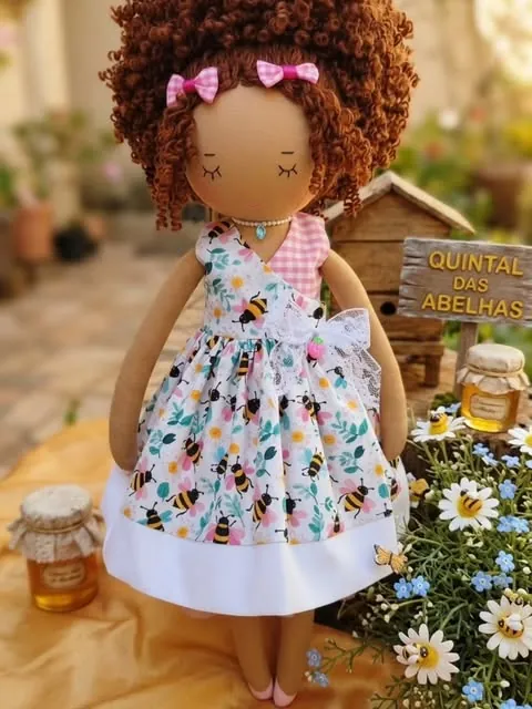 Boneca de cachos castanhos volumosos com laço rosa e vestido de abelhas
