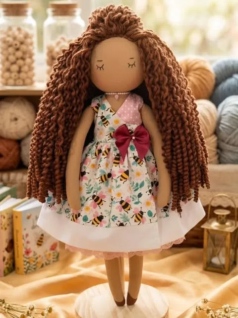 Boneca de cachos longos castanhos com vestido de abelhas e laço vermelho